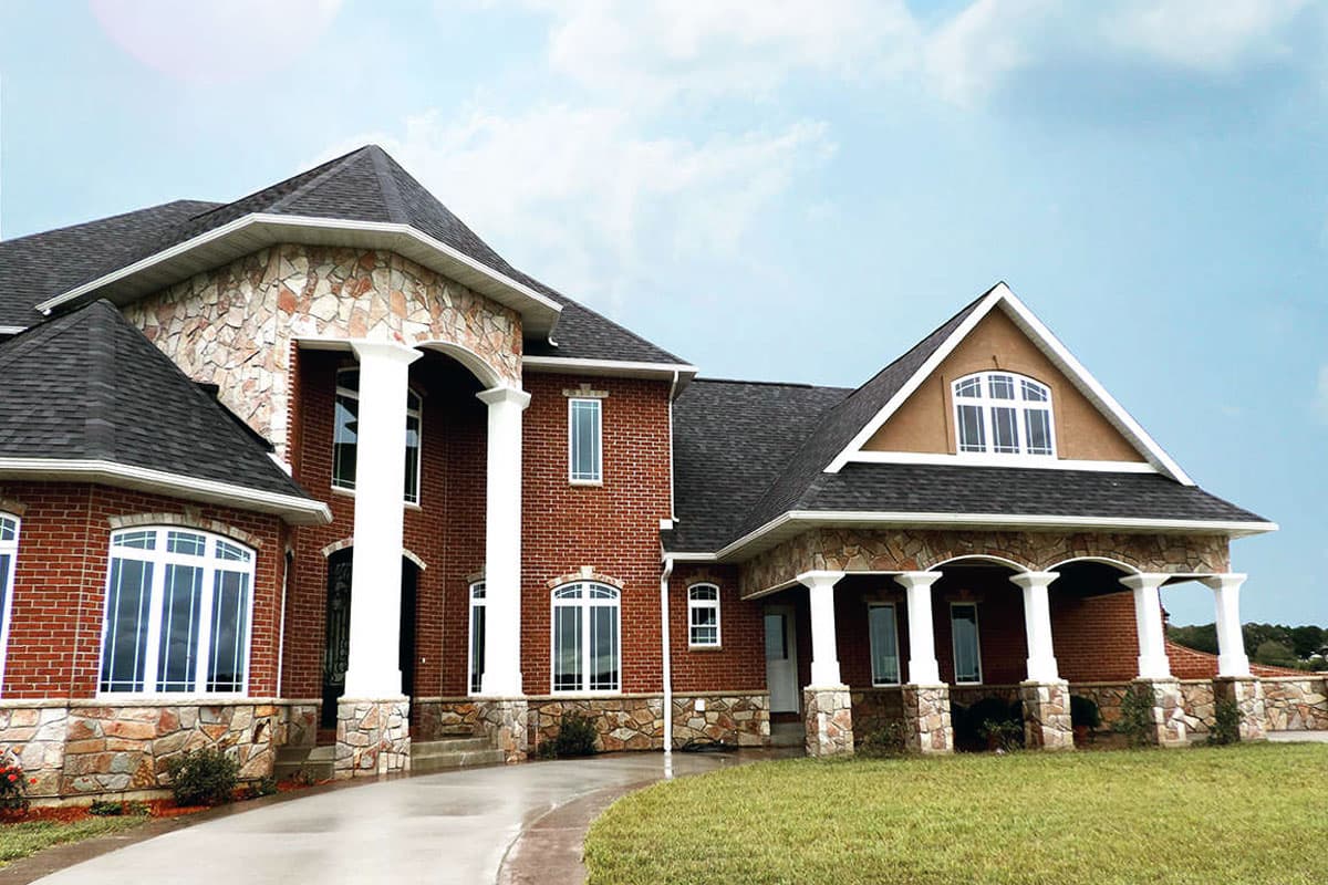 House plan exterior showing a two-story brick home with stone accents, a covered porch with columns, and multiple gables.