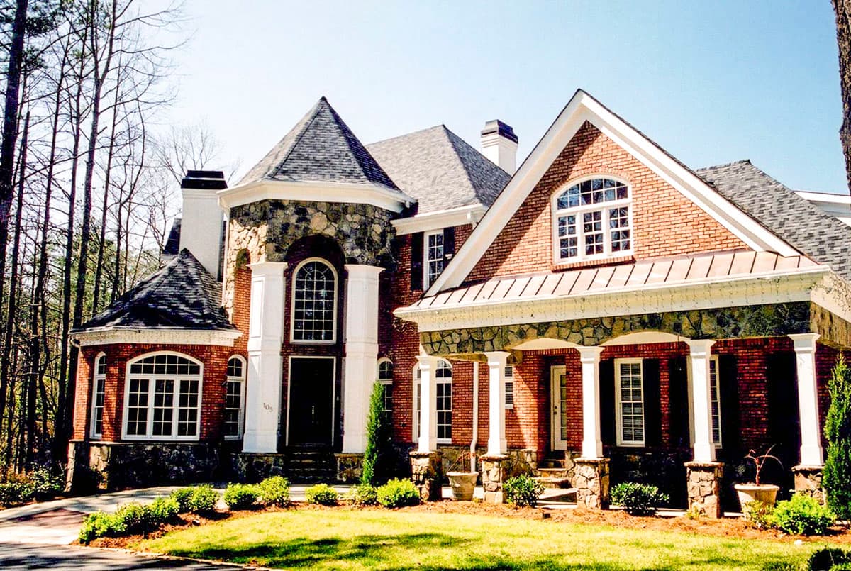 House plan exterior featuring brick facade, stone accents, multiple gables, arched windows, and covered porch with columns.
