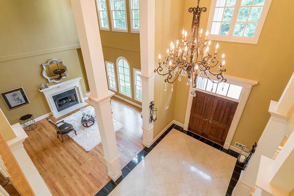 Interior view of a two-story foyer with a fireplace, chandelier, and double wooden doors.