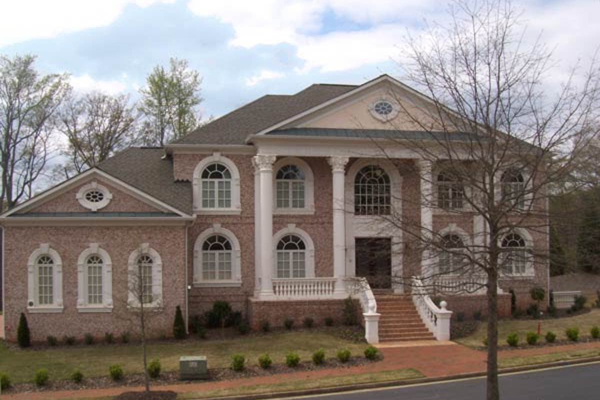Neoclassical house plan exterior with prominent portico, arched windows, and brick facade. Two stories visible.
