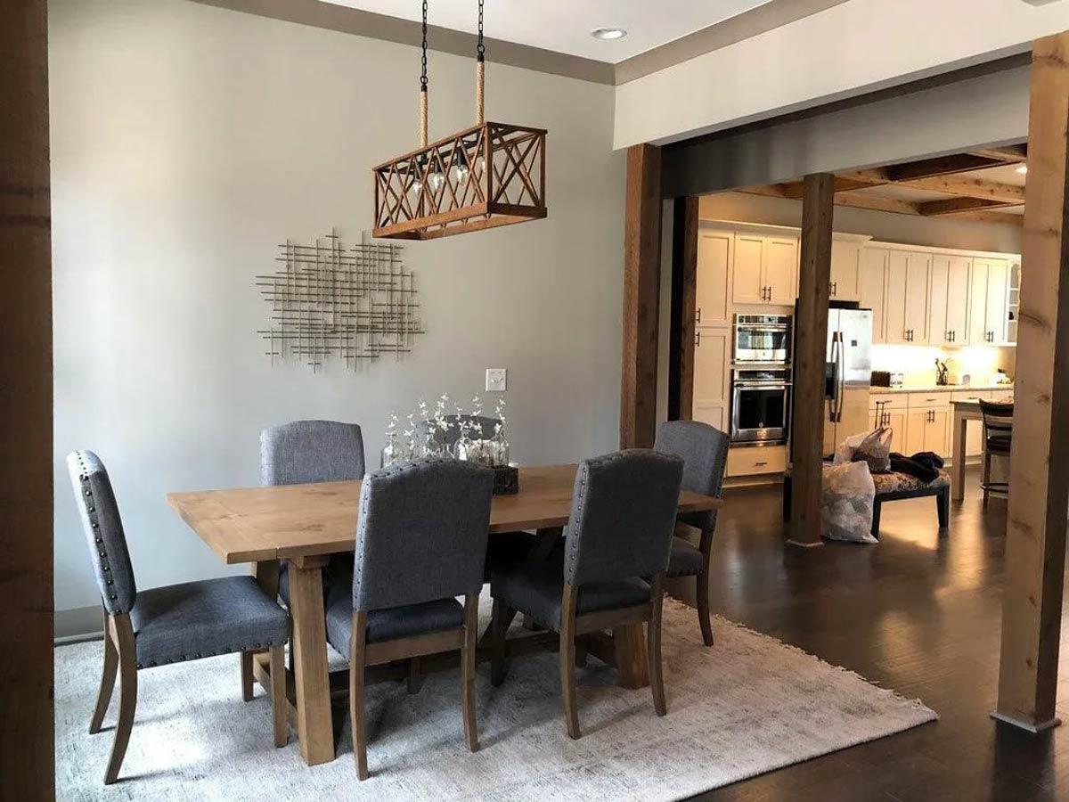 Dining area with wooden table and upholstered chairs adjacent to kitchen with white cabinetry and stainless steel appliances.