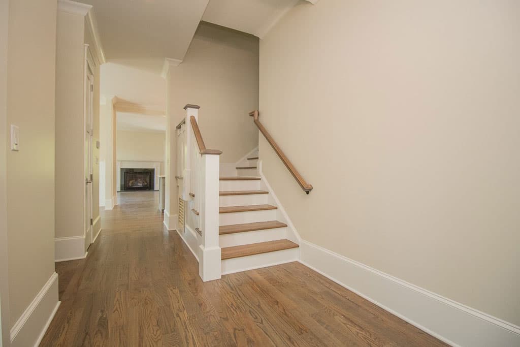 Interior hallway with hardwood floors and white staircase leading to upper level. Fireplace visible in distant room.