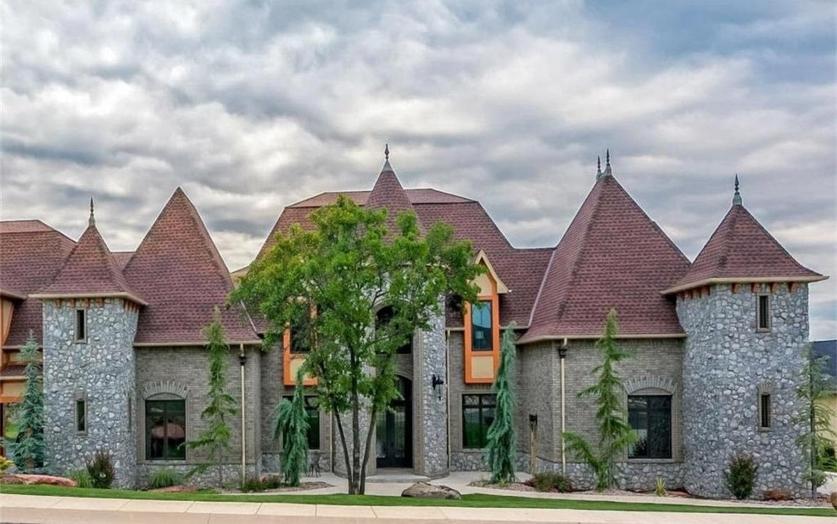House plan exterior with stone turrets, multiple gables, and a central arched entryway.