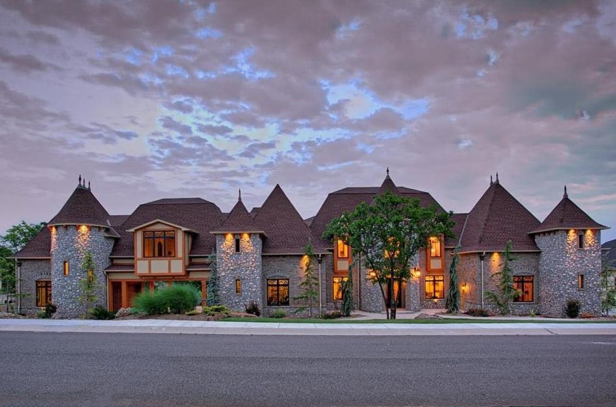 House plan exterior with stone facade, multiple turrets with conical roofs, and prominent gables.