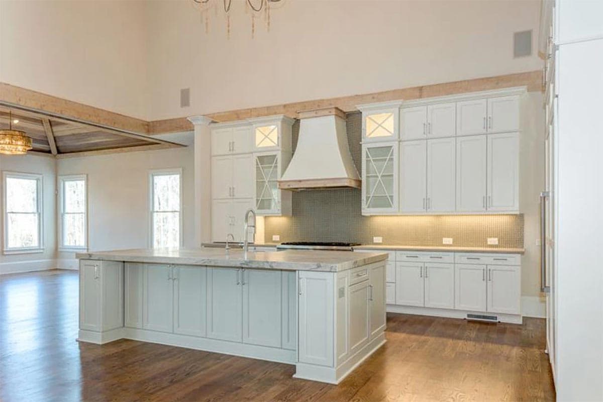 Modern kitchen with white cabinetry, large island with sink, decorative range hood, and vaulted ceiling with exposed beams.