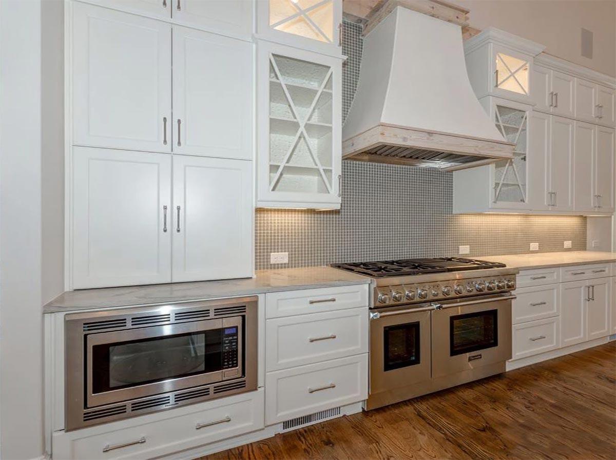 Kitchen with white Shaker cabinets, stainless steel microwave, range, and custom range hood with wood trim.