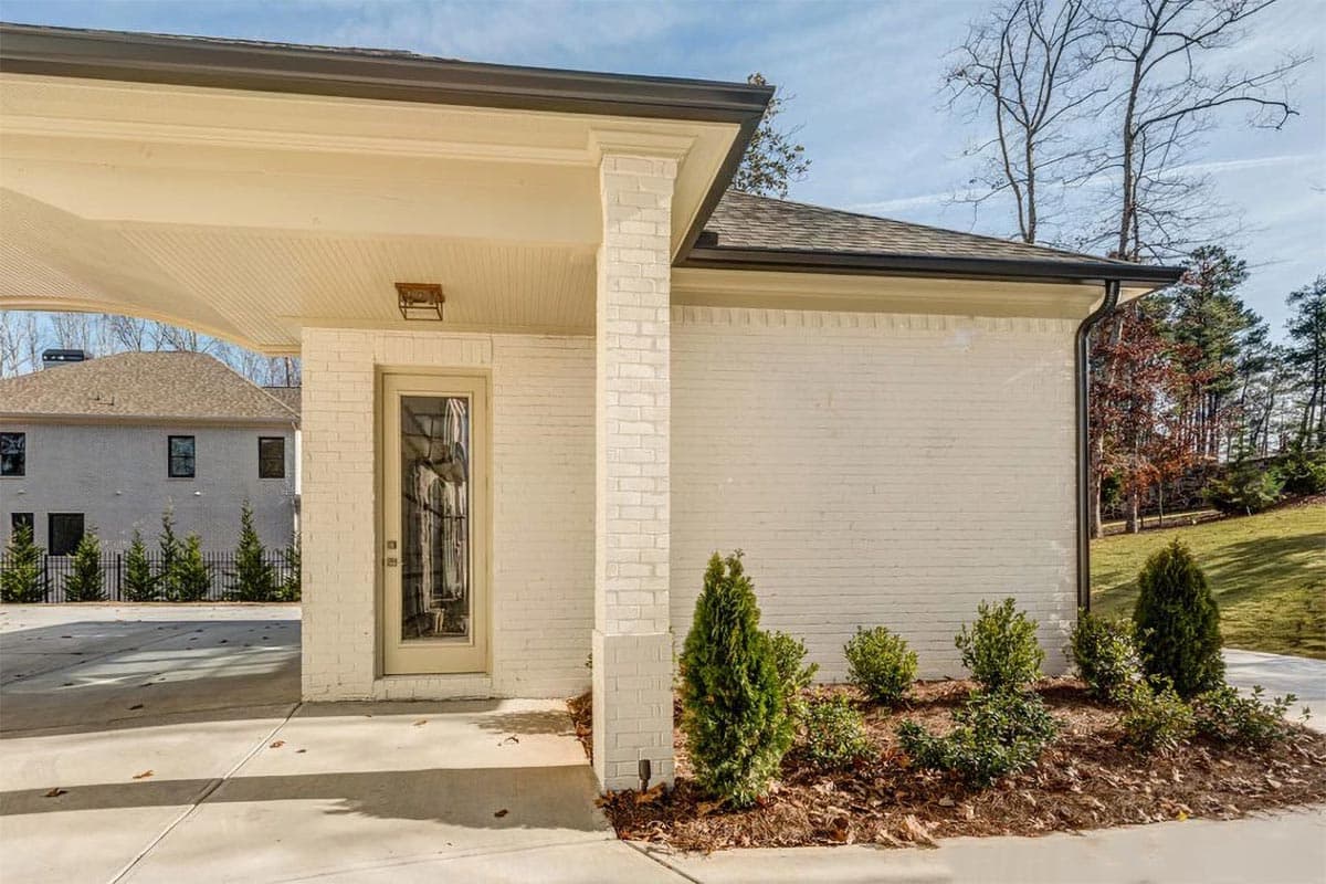 House plan exterior with white brick, covered entryway, and attached carport. Two stories visible in background.