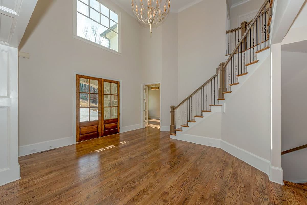 Interior foyer with grand staircase, double wooden doors, and a large window above.