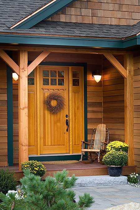 House plan exterior features wooden siding, a gabled roof, and a covered porch with wooden beams framing a multi-pane glass door.