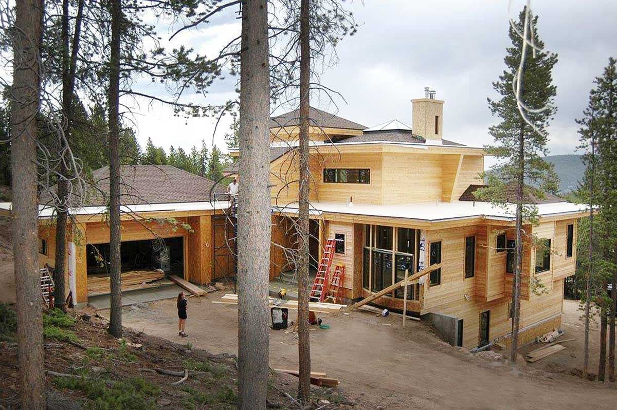 Modern house plan exterior under construction, featuring wood siding, multiple gables, and a three-car garage.