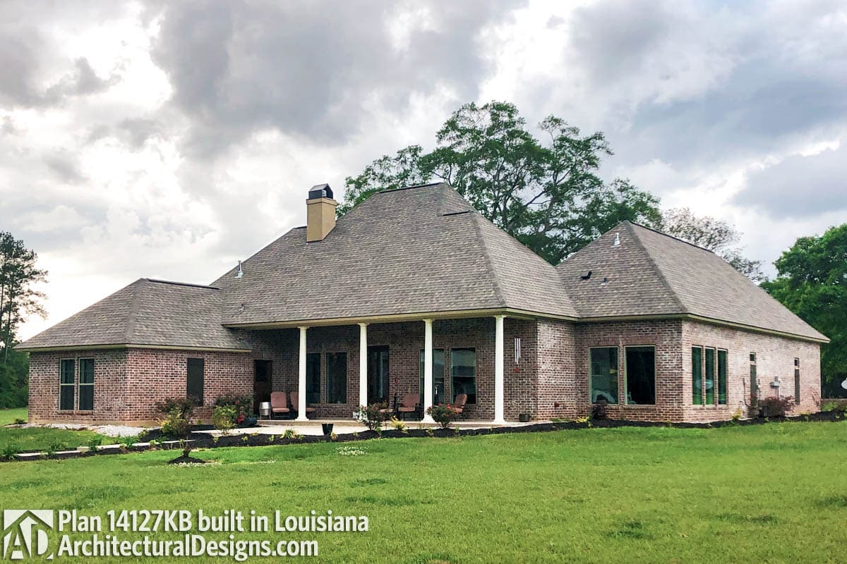 House plan exterior: One-story brick home with a covered porch supported by columns, multiple gables, and a prominent chimney.