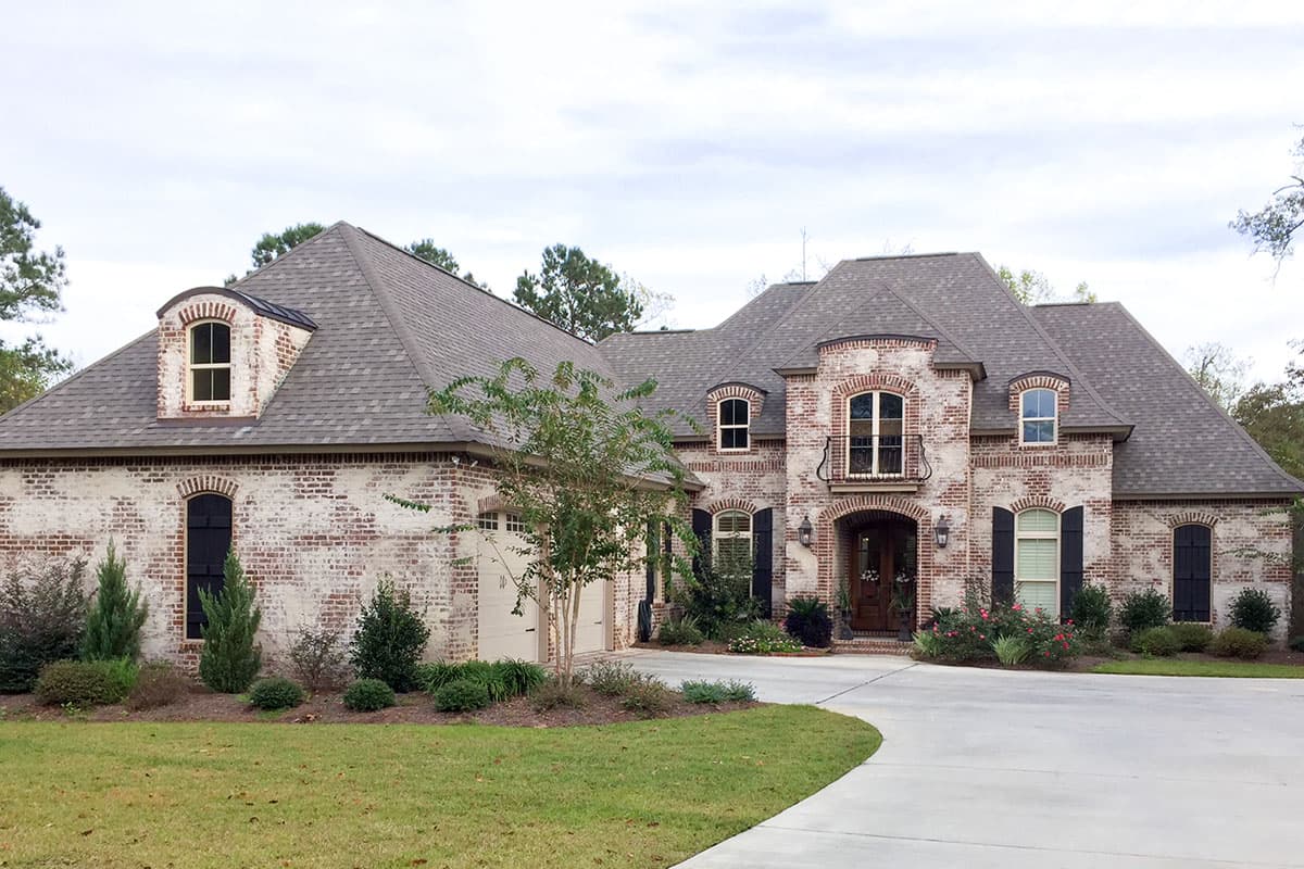 House plan exterior: French-inspired brick home with dormers, arched windows, covered entry, and a three-car garage.