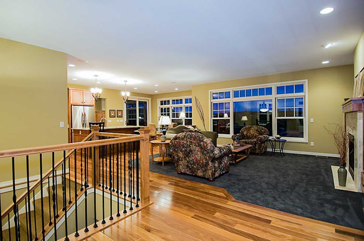 Open concept living area with fireplace, large windows, and a wooden staircase with black balusters.