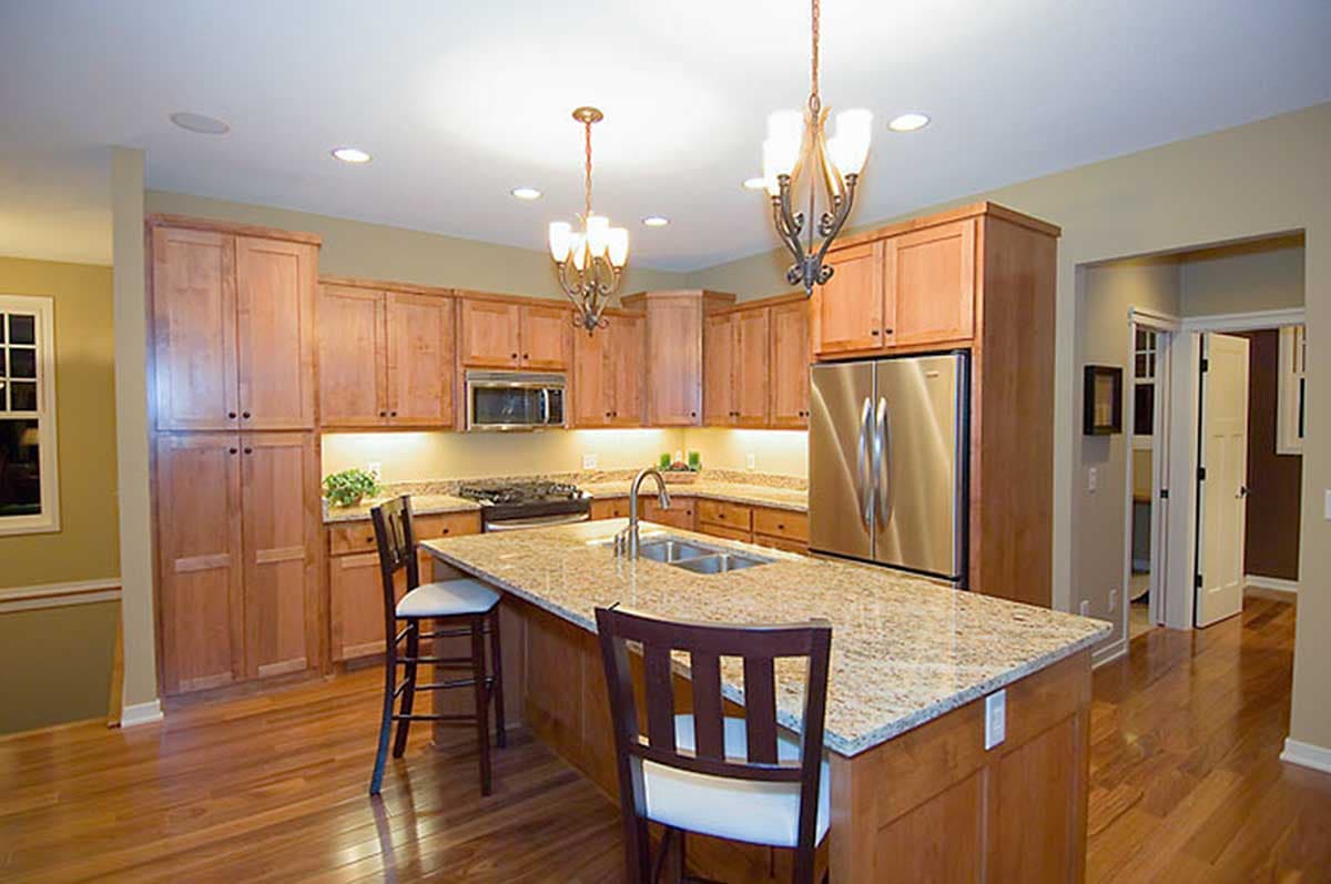 Kitchen with light wood cabinets, granite island with sink, stainless steel appliances, and pendant lighting.