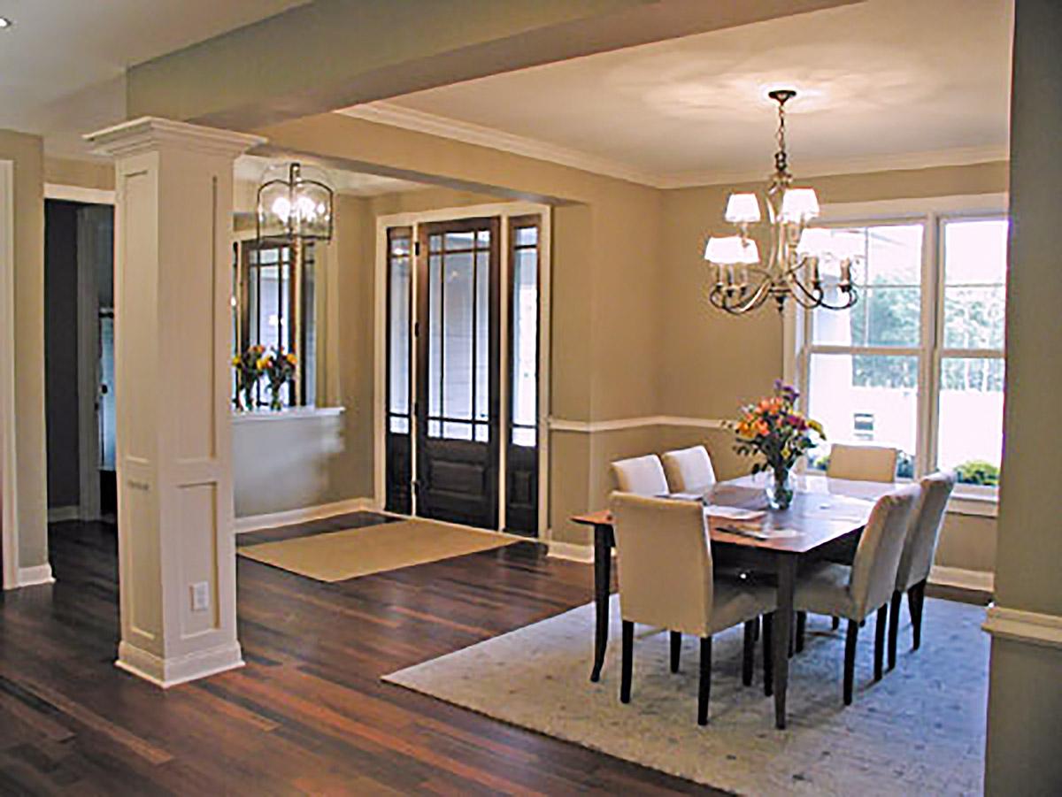 Interior view of a dining room with a table set for six, chandelier, and large windows. A decorative column defines the space.