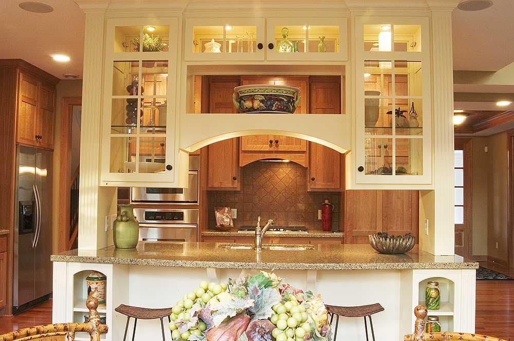 Kitchen interior with light cream cabinetry, glass display cabinets, granite countertop island, and stainless steel appliances.