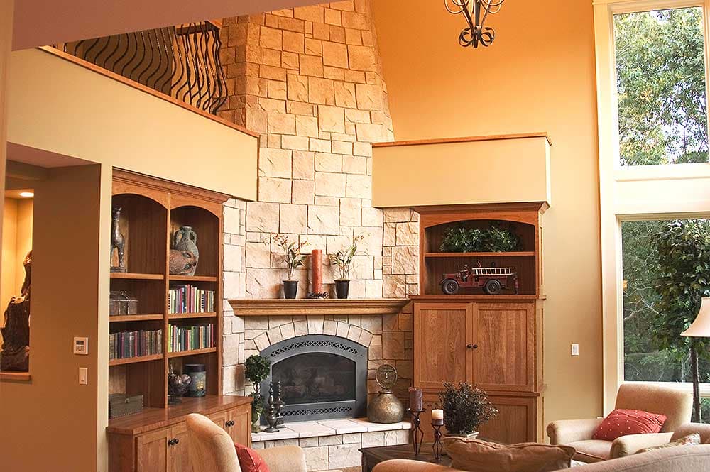 Interior view of a great room featuring a large stone fireplace, built-in bookshelves, and a second-story balcony with wrought iron railing.
