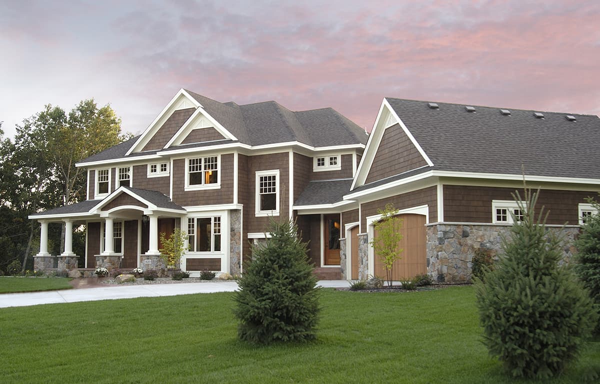 Two-story house plan exterior with a gabled roof, shingle siding, stone accents, and a covered front porch with white columns.