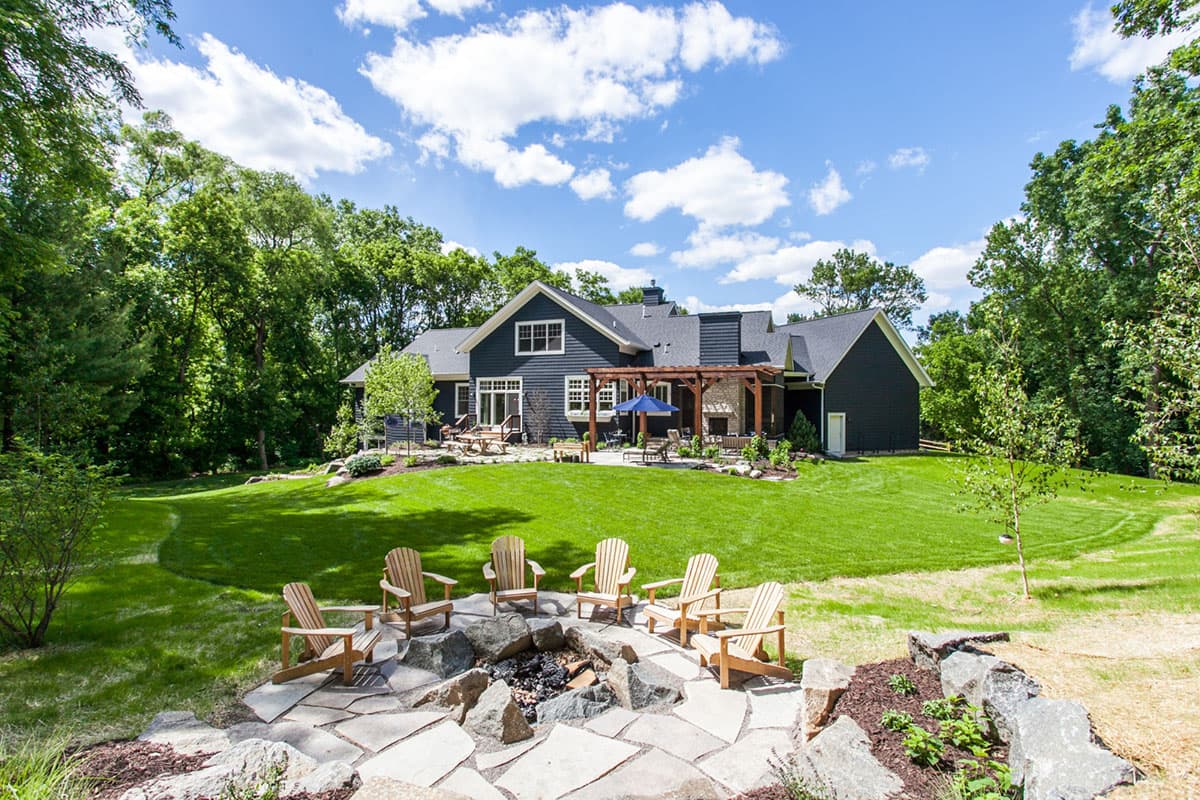 Modern Farmhouse house plan exterior with dark siding, gables, dormers, pergola, and stone fireplace.
