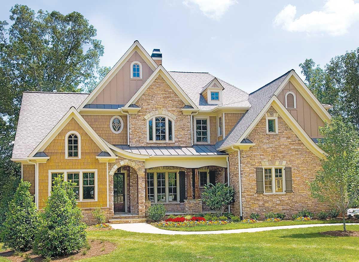 House plan exterior: Two-story home with stone and shingle siding, arched entryway, multiple gables, and dormer windows.