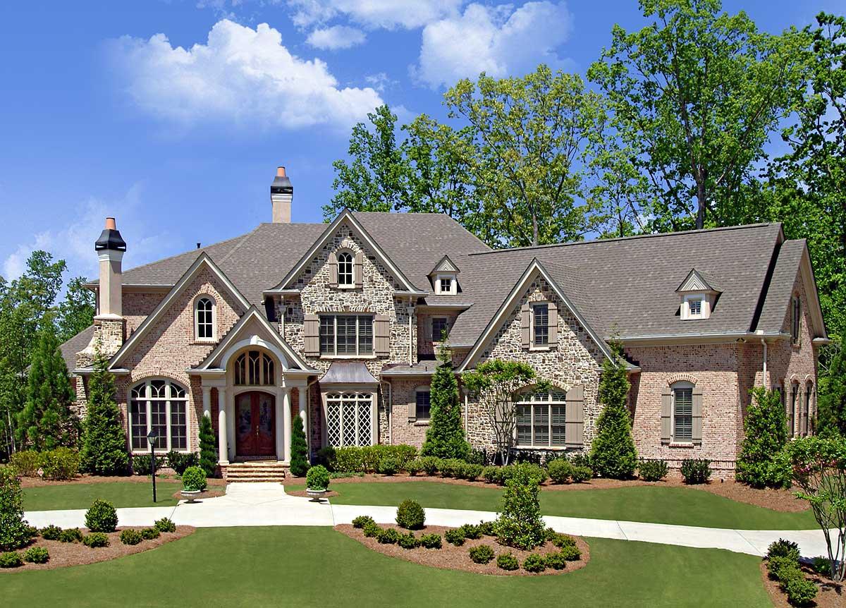 House plan exterior featuring a multi-story brick and stone facade, arched entryway, multiple gables, dormers, and a layered roofline.