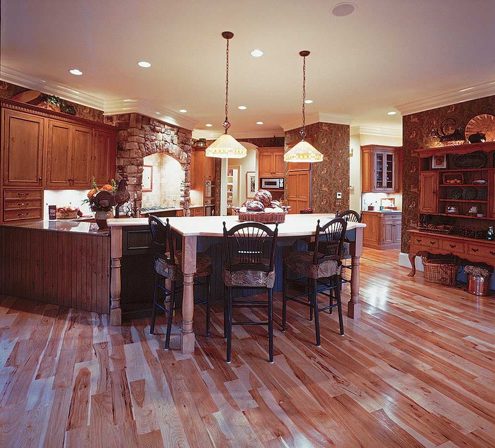Kitchen interior with a large island, stone fireplace, wood cabinetry, and pendant lighting.