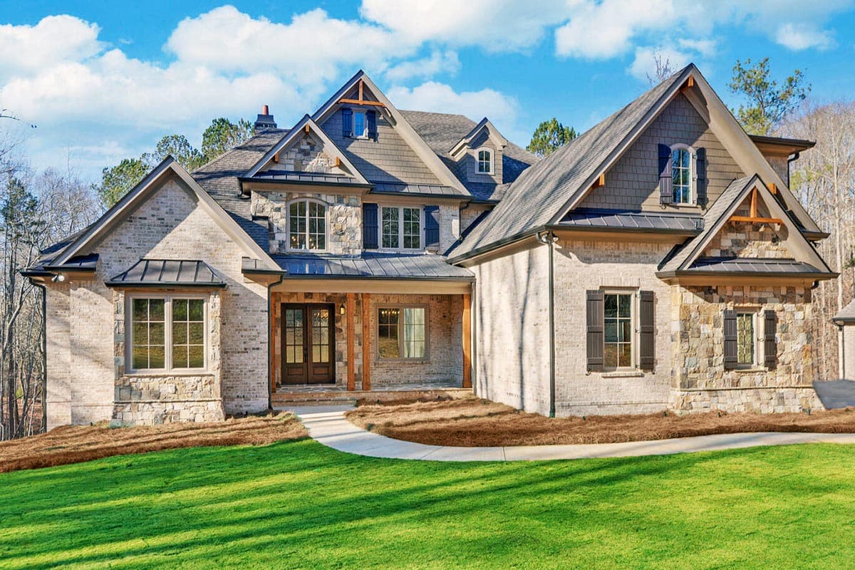 House plan exterior. Two-story home with a stone and brick facade, multiple gables, and a covered porch. Features include a mix of window styles.
