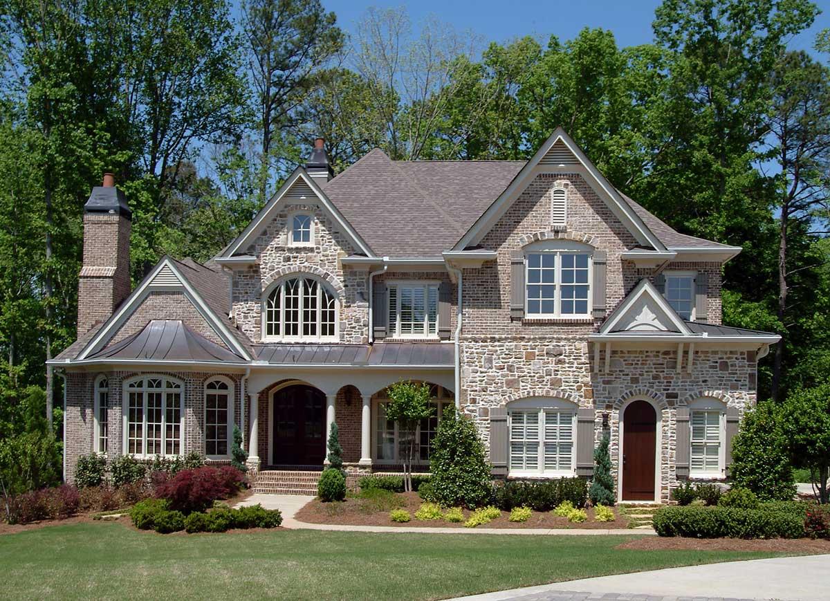 House plan exterior with arched windows, stone and brick facade, dormers, and covered entry with columns.