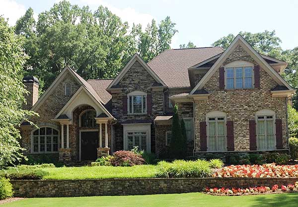 Two-story house plan exterior with stone and brick facade, arched entryway, multiple gables, and dormer windows.