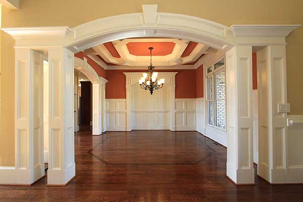 Interior view of a dining room with arched doorway, coffered ceiling, chandelier, wainscoting, and large windows.