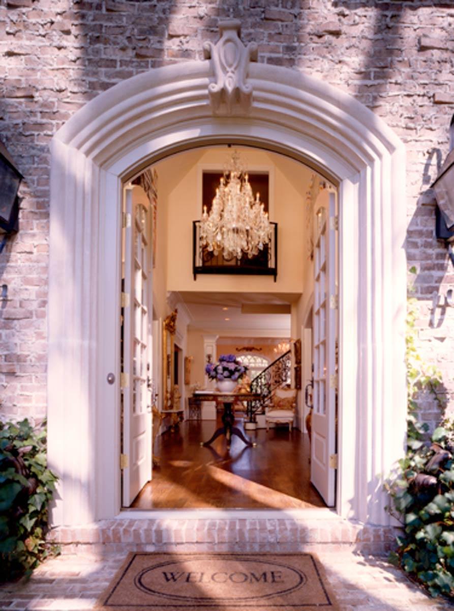 Entrance to foyer with arched entryway, chandelier, and ornate staircase visible.