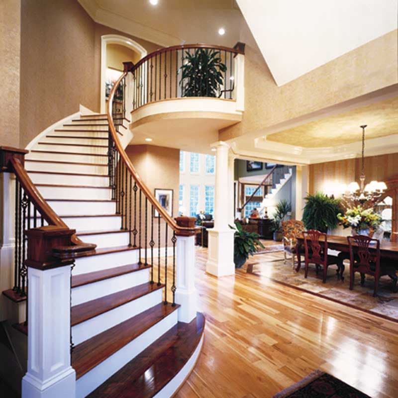 Interior view of a grand foyer with a curved staircase, balcony overlooking the entrance, and a dining room.
