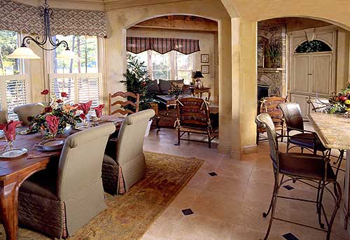 Dining room with table set for meal, opening to living area and kitchen with island and fireplace.