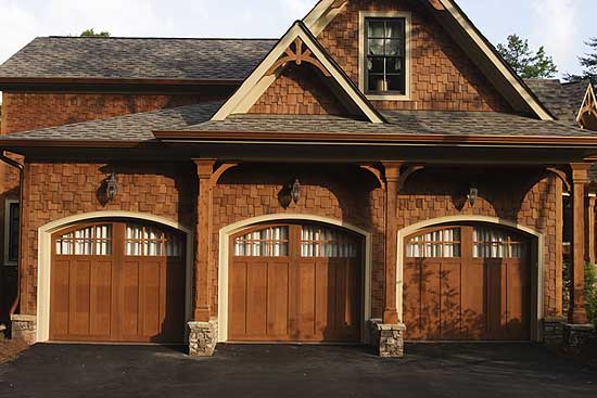 House plan exterior: three-car garage with arched wooden doors, shingle siding, and decorative gable detail.
