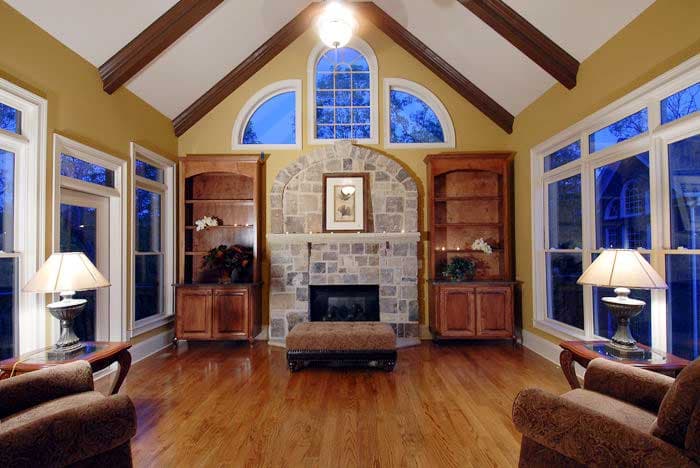 Great room with vaulted ceiling, exposed beams, stone fireplace, built-in bookcases, and arched windows.