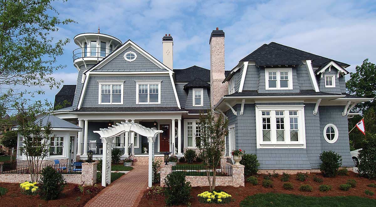 House plan exterior: gray shingle siding, dormers, prominent chimneys, and a circular tower with a balcony.