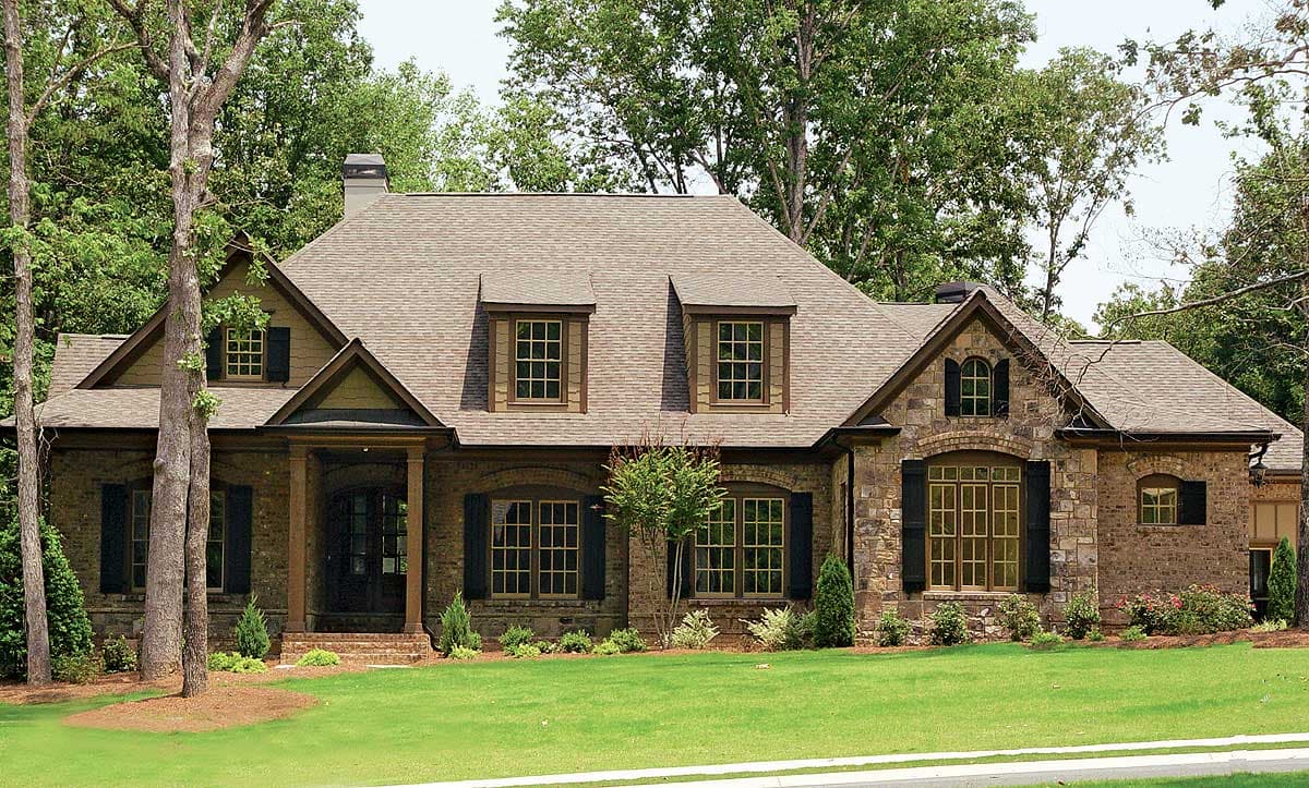 House plan exterior: Two-story dwelling with brick and stone facade, prominent gables, dormer windows, and covered entry porch.