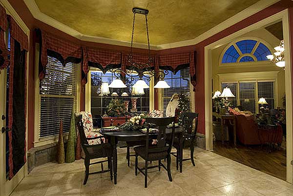 Dining room with bay windows, chandelier, and view into a living area with arched window.