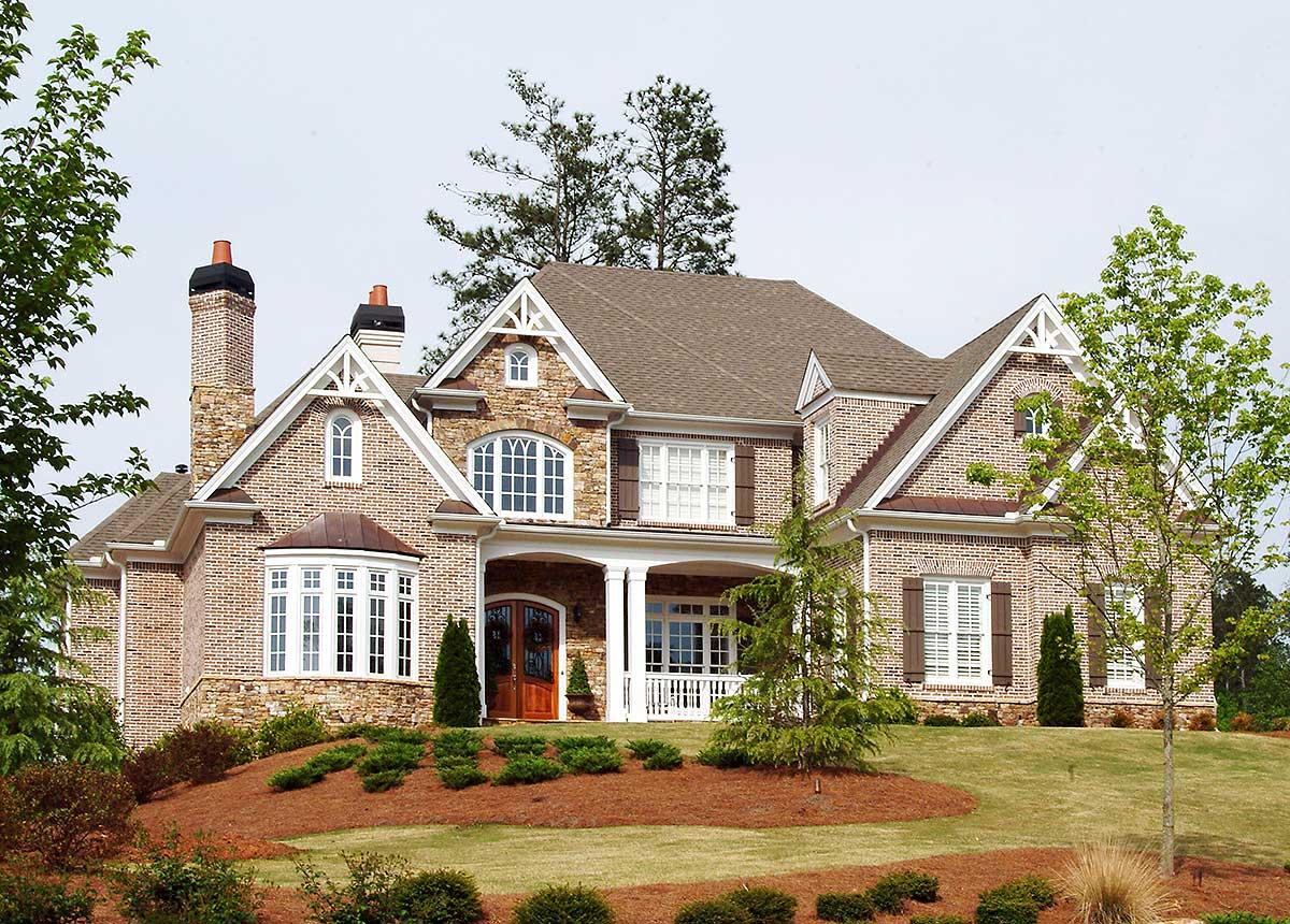 House plan exterior: Brick home with stone accents, arched windows, prominent gables, and a covered front porch with columns.