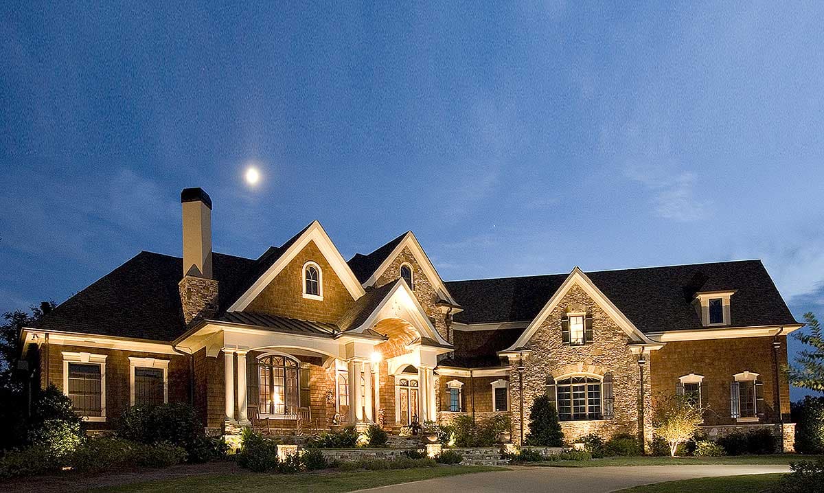 House plan exterior: Two-story home with stone and wood facade, multiple gables, arched dormer, and covered front porch with columns.