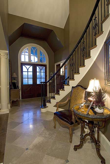 Foyer with arched double doors, curved staircase with wrought iron balusters, and patterned marble flooring.