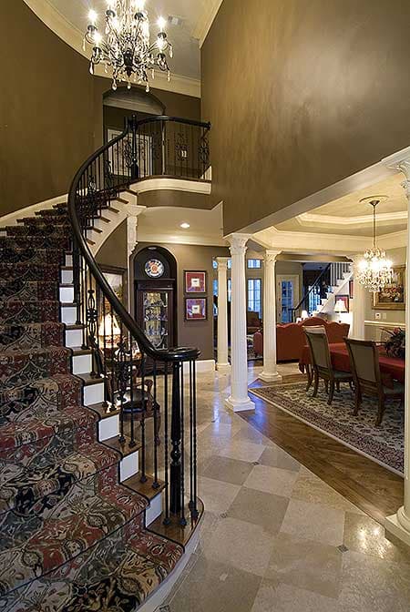 Grand foyer with curved staircase, chandelier, columns, and dining room visible.