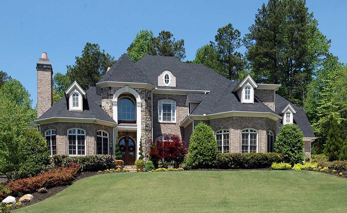 House plan exterior featuring stone and brick facade, arched entryway, multiple gables, dormers, and a prominent brick chimney.