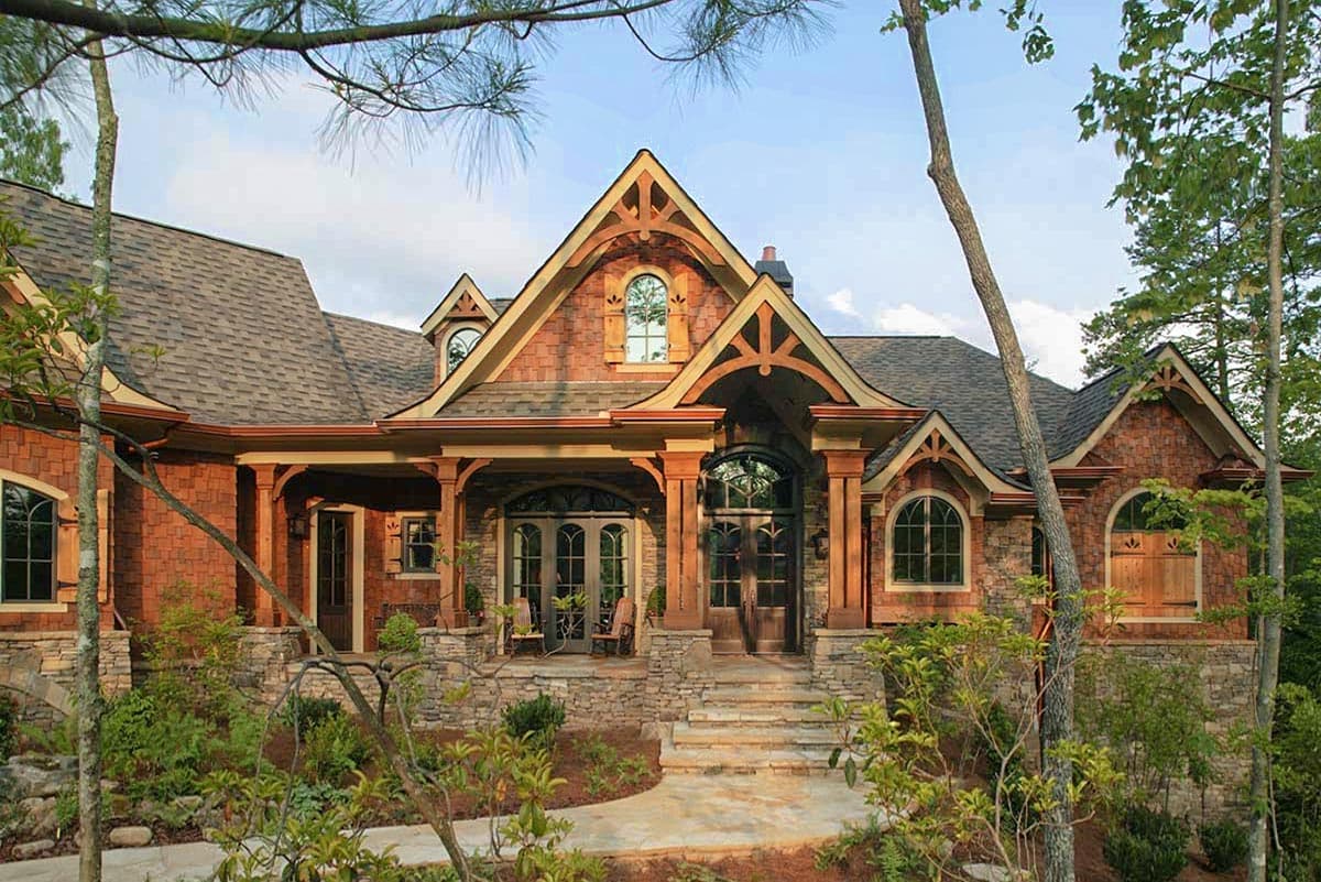 House plan exterior. Rustic style, two stories, stone base, wood shake siding, covered entry with decorative trusses, arched windows.