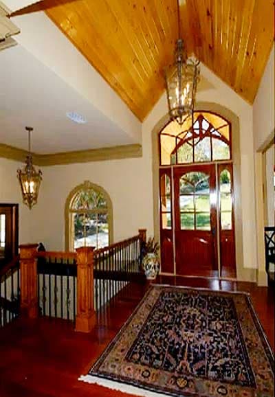 Entryway with vaulted wood ceiling, ornate double door with arched stained glass transom, and wood staircase with metal balusters.