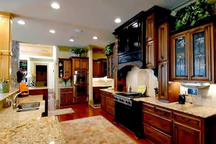 Kitchen with granite countertops, dark wood cabinetry, double ovens, and a stainless steel range with ornate hood.