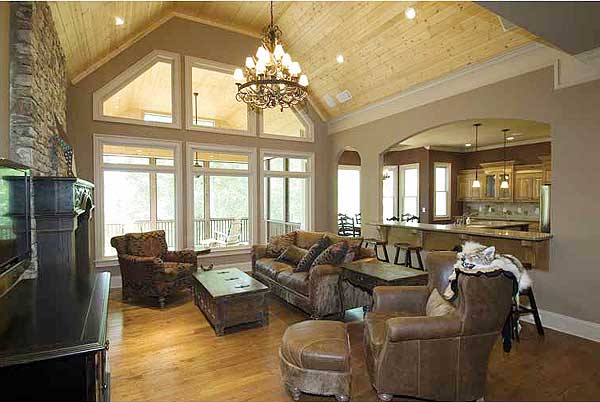 Vaulted ceiling living room with stone fireplace, large windows, and view of kitchen with island.