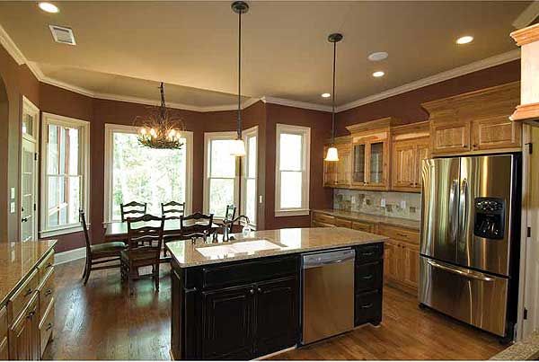 Kitchen with island, stainless steel refrigerator, wood cabinets, dining area with bay window, and chandelier.