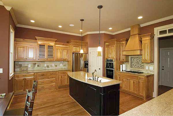 Kitchen with natural wood cabinets, large island with sink, stainless steel refrigerator, and range with wood hood.