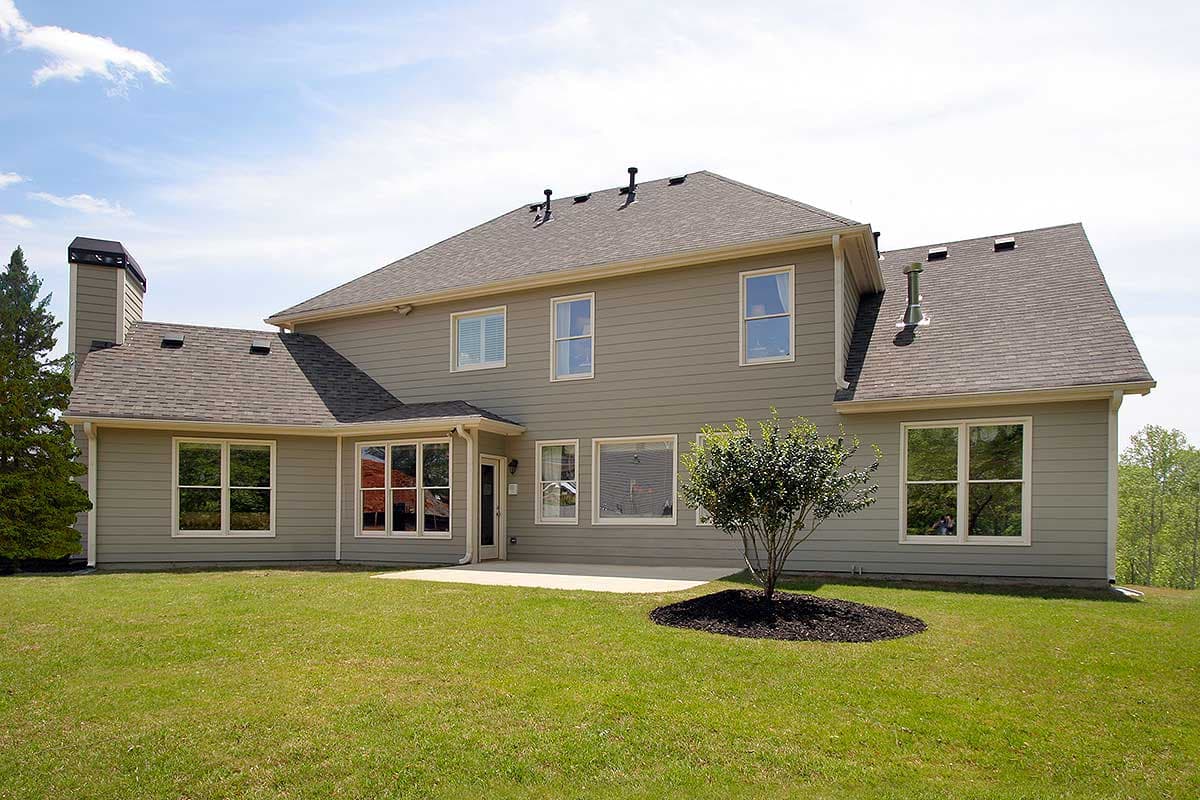 House plan exterior: Two-story dwelling with a prominent chimney, gable rooflines, multiple windows, and a patio.